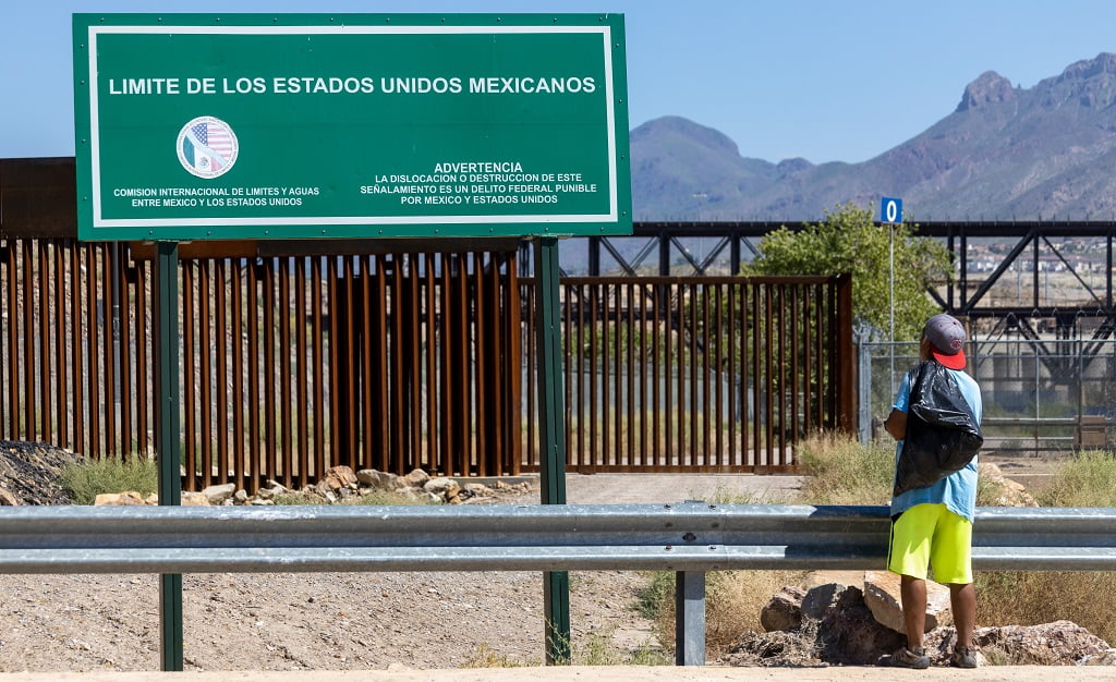 Migrant stands at the border with large green sign that reads no entry